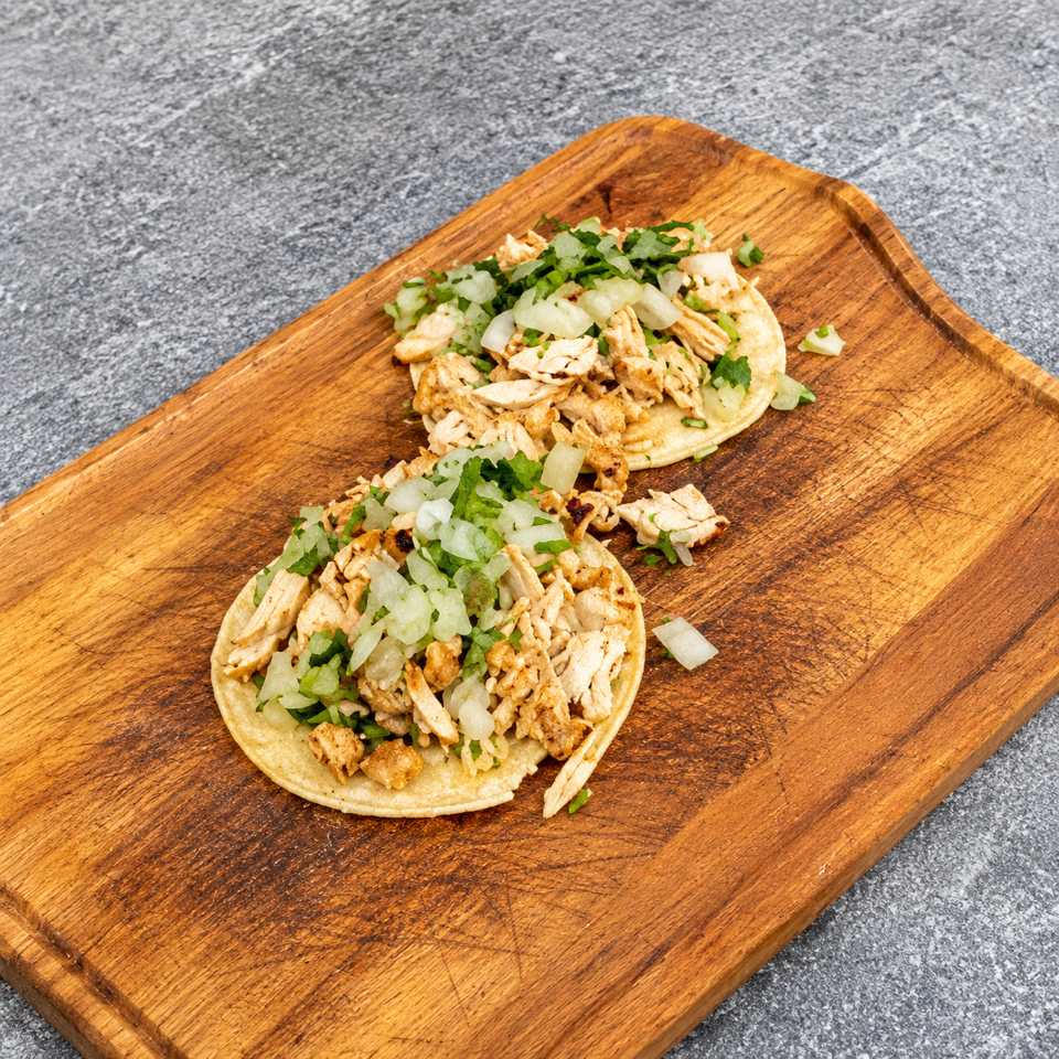 Two chicken tacos topped with chopped onions and cilantro on a wooden serving board.