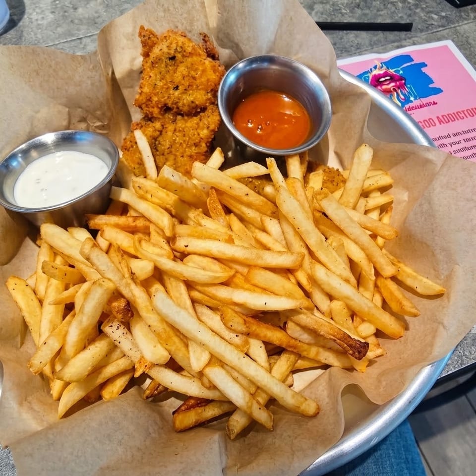 Basket of golden fries with fried fish, creamy dipping sauce, and orange sauce on a paper-lined tray.